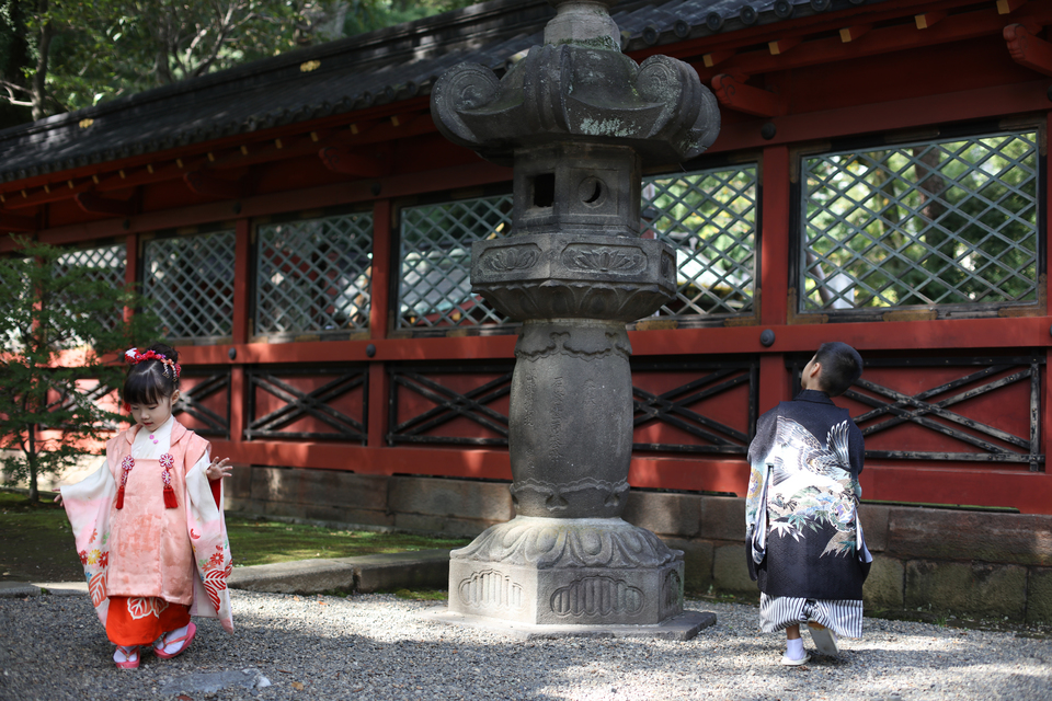 根津神社の境内で、光降り注ぐ緑をバックに、走り回る３歳と５歳の子供たちを、東京都文京区千駄木のフォトスタジオ、ケープルヴィル写真館のフォトグラファーが写真を撮る。